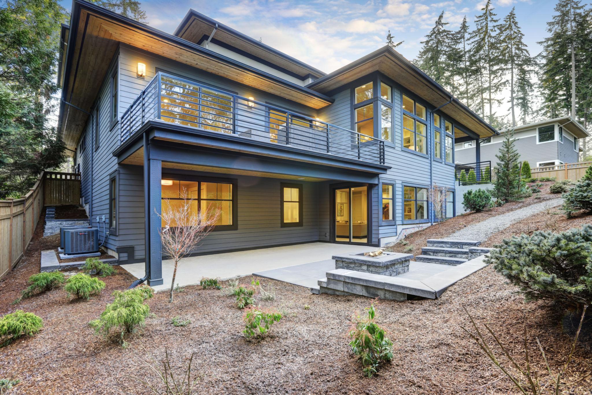 Modern two-story house with large windows and spacious patio—contact us to tour the landscaped yard with trees.